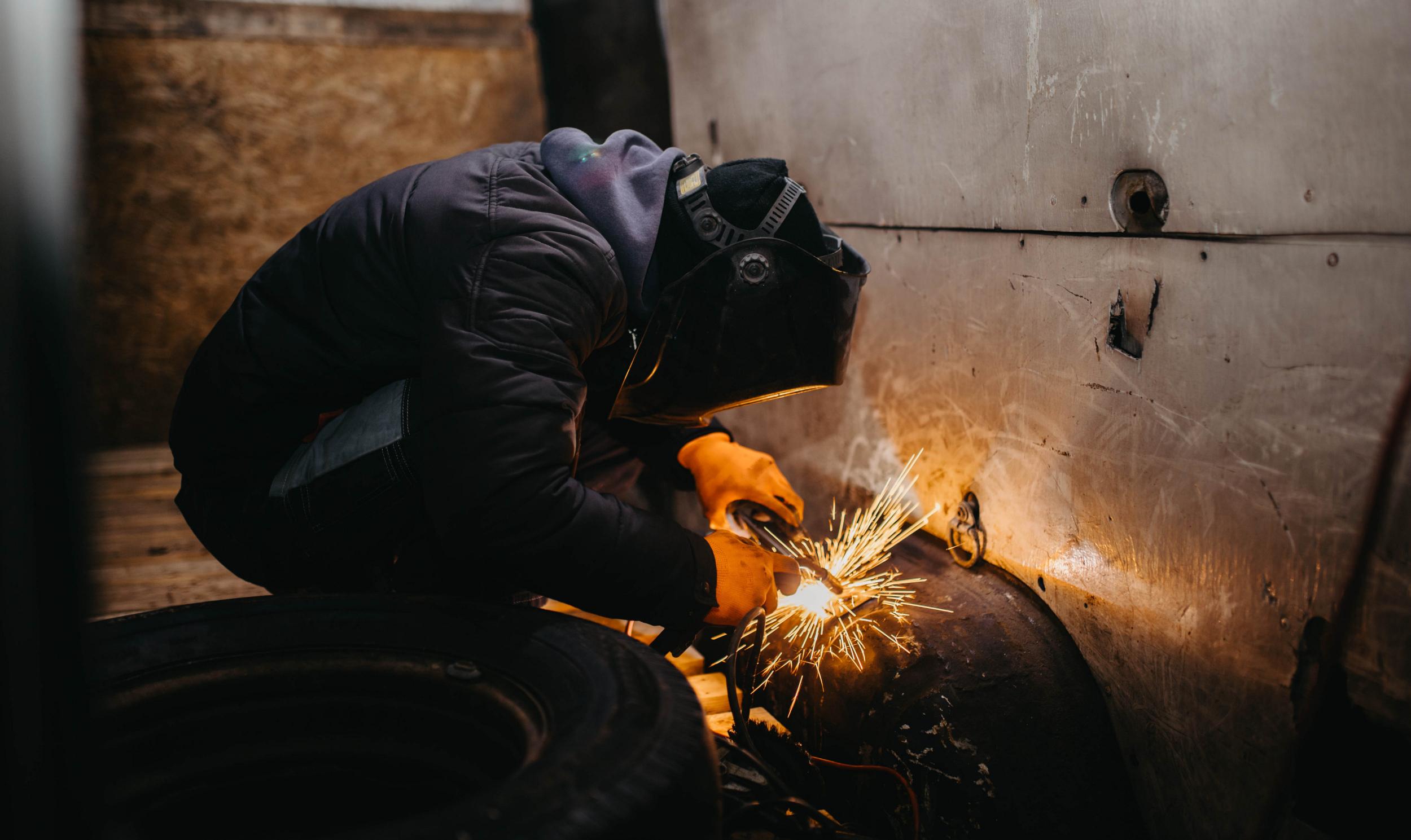 worker man in a welding mask welds metal in the back of a van